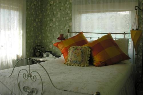 Cozy bedroom with a floral green wallpaper, a white bed adorned with colorful pillows, and soft natural light.