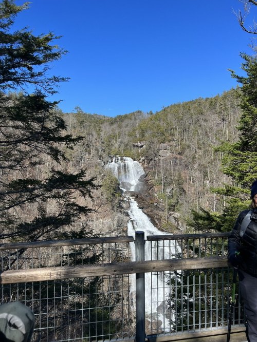 A scenic view of a waterfall cascading down a rocky cliff, surrounded by trees under a clear blue sky.