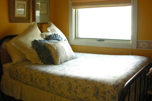 Cozy bedroom with a single bed, floral bedding, and decorative pillows against a yellow wall and window.