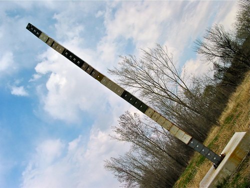A tall, vertical metal structure with numbered plates, set against a cloudy sky and bare trees in the background.