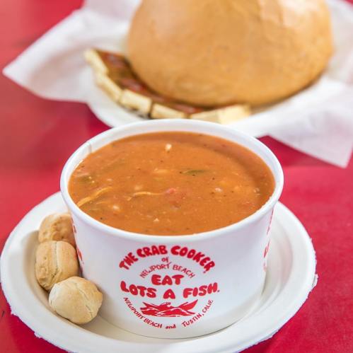 A bowl of seafood soup with a side of bread rolls on a red table.
