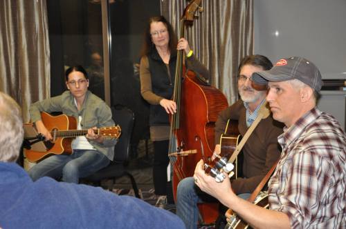 A group of musicians playing instruments, including guitars and a double bass, in a cozy indoor setting.