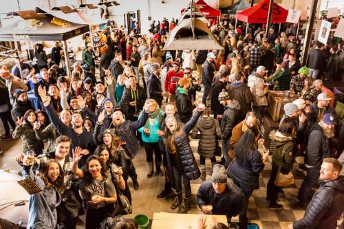 A lively crowd of people enjoying a festive event indoors, with many smiling and waving at the camera.