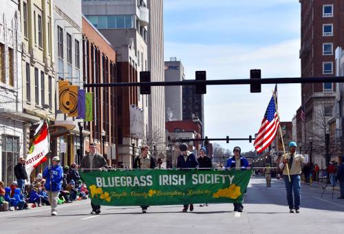 A parade featuring a banner for the Bluegrass Irish Society, with participants and spectators along the street.
