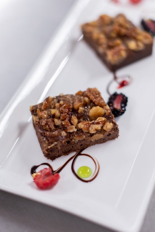 A close-up of a chocolate dessert topped with nuts, drizzled with sauces, served on a white plate.