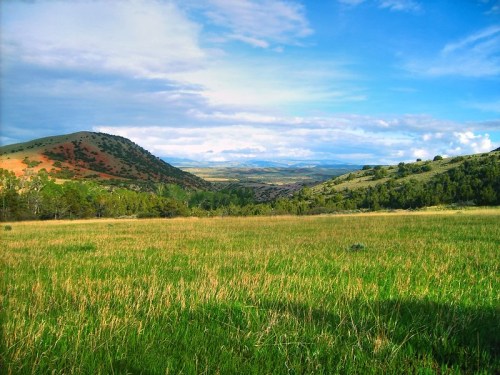 A scenic landscape featuring rolling hills, green grass, and a blue sky with scattered clouds.