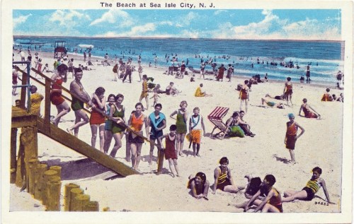 A vintage postcard depicting a busy beach scene at Sea Isle City, NJ, with people sunbathing and playing in the water.