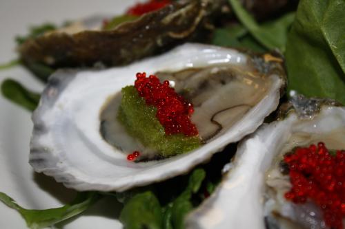 Close-up of oysters topped with green paste and red caviar, served on a bed of greens.