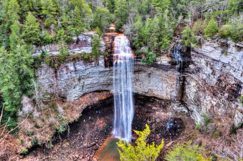 A stunning waterfall cascades down rocky cliffs, surrounded by lush green trees and a serene pool below.