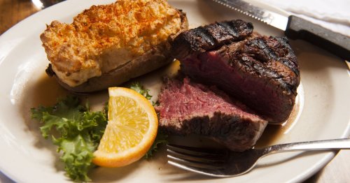 A plate featuring a grilled steak, a stuffed baked potato, a slice of lemon, and a bed of lettuce.