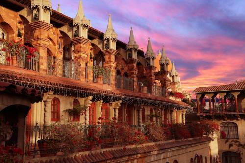A picturesque building with ornate architecture and balconies, set against a vibrant sunset sky.