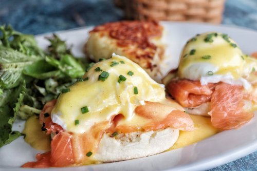 A plate of eggs Benedict with smoked salmon, hollandaise sauce, and a side of greens and hash browns.