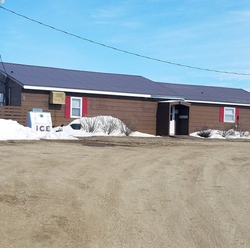 A brown building with red accents, snow on the ground, and an "ICE" sign outside under a clear blue sky.