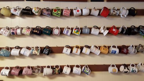 A wall display of various coffee mugs arranged in rows, showcasing different designs and colors.