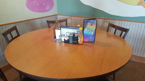 A round wooden table set for dining, featuring menus, condiments, and a colorful wall mural in the background.