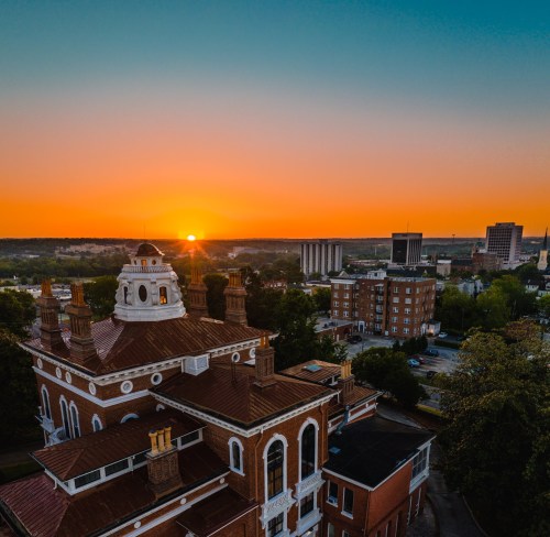 Aerial view of a historic building at sunset, with a vibrant sky and city skyline in the background.