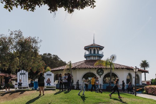A lively park scene with people enjoying the day near a charming building with a tower and palm trees.