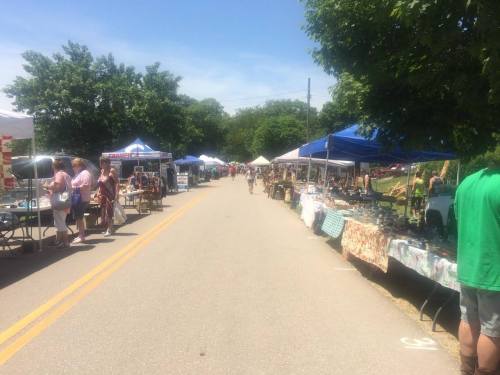 A vibrant outdoor market with colorful tents and stalls lining a sunny street, filled with people browsing goods.