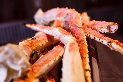 A close-up of cooked crab legs with a reddish hue, arranged on a dark surface.