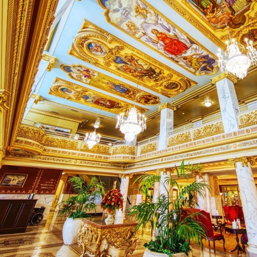 Luxurious hotel lobby with ornate ceilings, chandeliers, and elegant decor, featuring lush plants and floral arrangements.