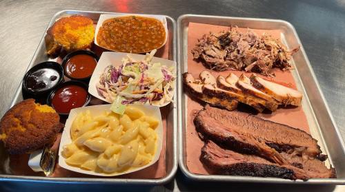 A tray of barbecue featuring brisket, pulled pork, macaroni and cheese, coleslaw, baked beans, cornbread, and sauces.