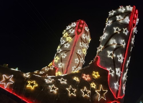 Giant illuminated cowboy boots adorned with colorful stars, glowing against a night sky.