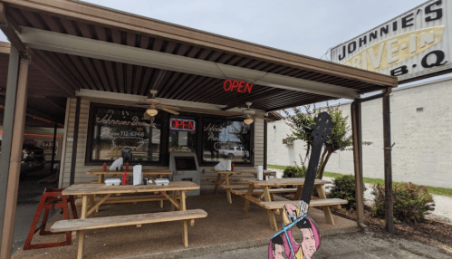 Exterior of Johnnie's Drive-In BBQ with an "OPEN" sign, picnic tables, and a colorful guitar decoration.