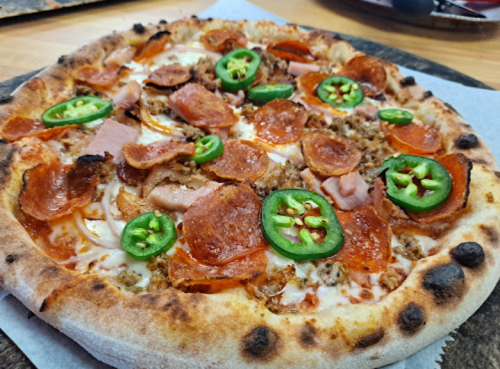 A close-up of a pizza topped with pepperoni, ham, jalapeños, and melted cheese on a golden crust.