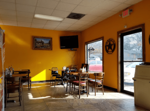 Brightly lit restaurant interior with orange walls, tables, and chairs, featuring a TV and large windows.
