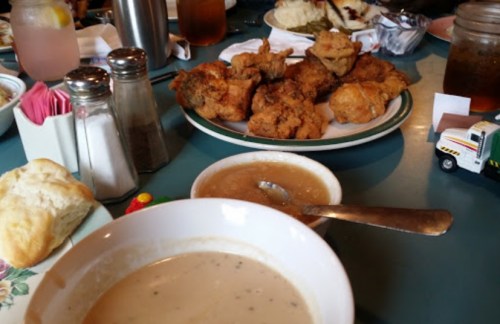 A table spread with fried chicken, a bowl of gravy, a biscuit, and drinks in a casual dining setting.