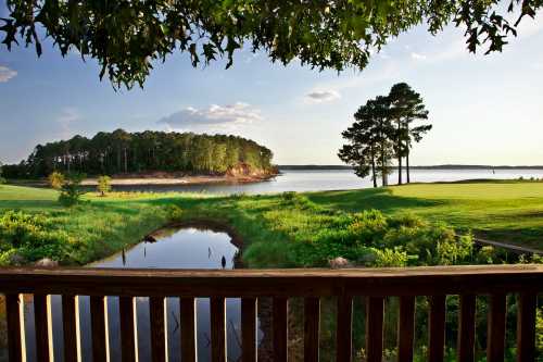 Scenic view of a lake surrounded by trees and greenery, with a wooden railing in the foreground.