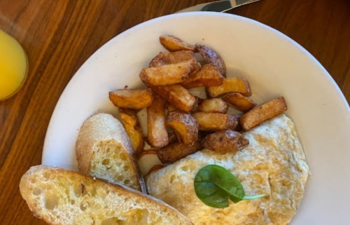 A plate with an omelette, golden potato wedges, and two slices of garlic bread, garnished with a leaf.