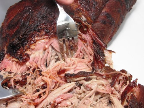 A close-up of pulled pork being served, with a fork lifting tender, shredded meat from a larger piece.