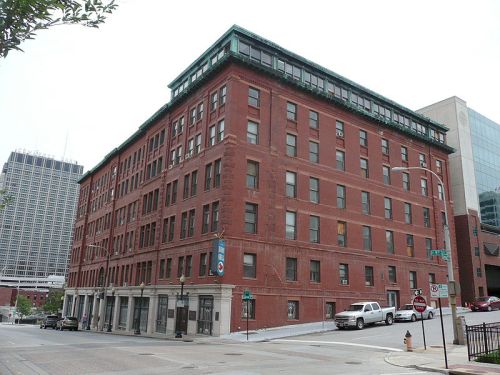 Historic red brick building with a green roof, located at a street corner in an urban setting.