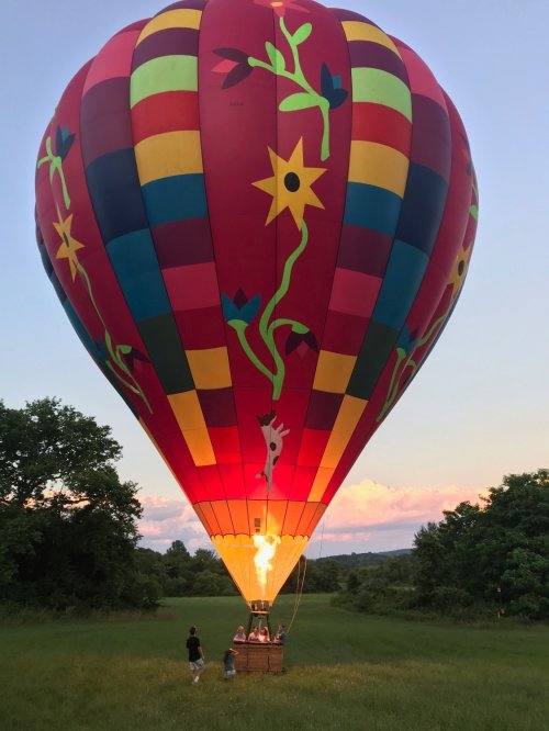 A colorful hot air balloon is being prepared for flight in a grassy field at sunset, with people nearby.