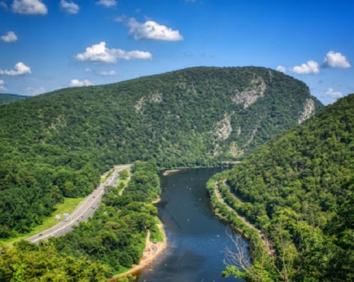 A scenic view of a river winding through lush green hills under a blue sky with fluffy clouds.