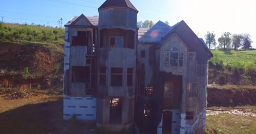 An abandoned, weathered house with a tower, surrounded by greenery and blue skies.