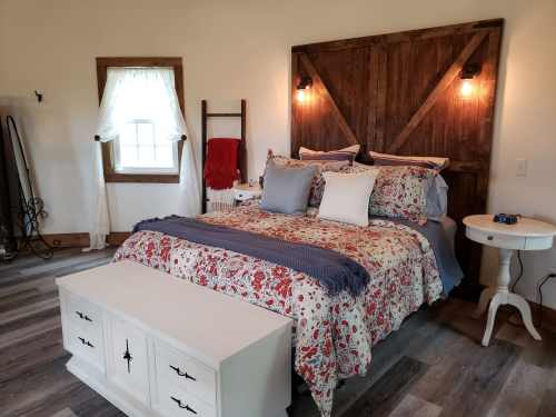 Cozy bedroom featuring a floral bedspread, wooden accent wall, and a white storage bench at the foot of the bed.