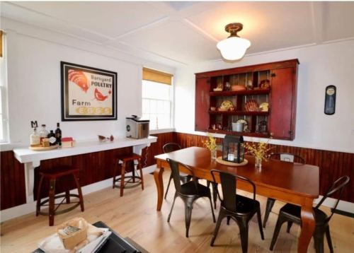 Cozy dining area with a wooden table, chairs, and a vintage poultry poster on the wall. Warm, inviting atmosphere.