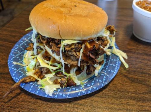 A stacked sandwich with pulled meat, lettuce, and sauce on a bun, served on a blue paper plate.
