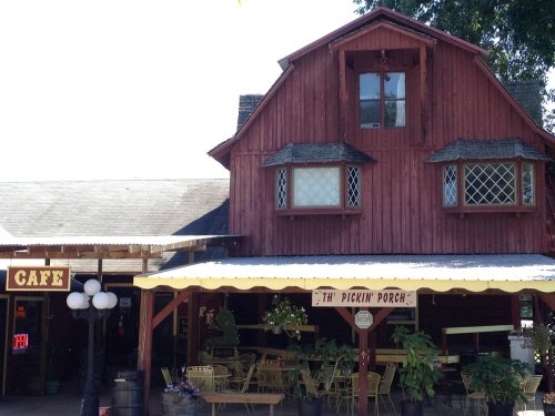 A rustic red barn-style building with a café sign and outdoor seating under a canopy.