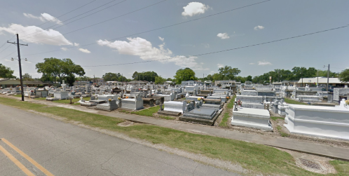 A wide view of a cemetery with numerous gravestones and monuments under a partly cloudy sky.