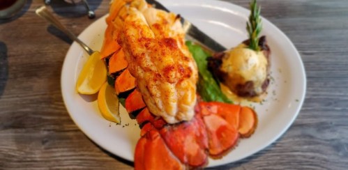 A plate featuring a large lobster tail, lemon wedges, and a side of baked potato with herbs.