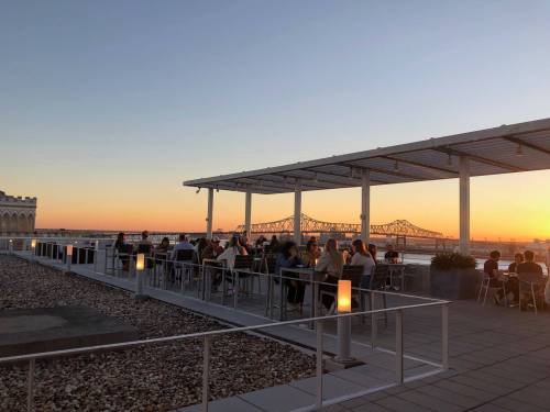 People dining on a rooftop terrace at sunset, with a bridge visible in the background.