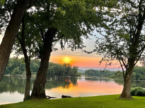 A serene sunset over a calm river, framed by trees and reflecting vibrant colors on the water's surface.