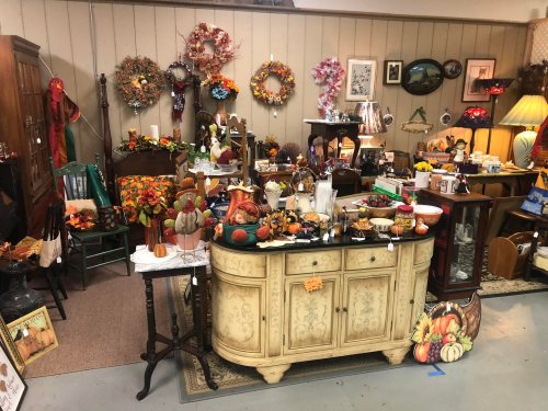 A cozy shop display filled with autumn decorations, vintage items, and seasonal decor, including wreaths and pumpkins.