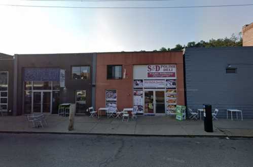 A street view of S&D Polish Deli with outdoor seating, flanked by two other buildings.