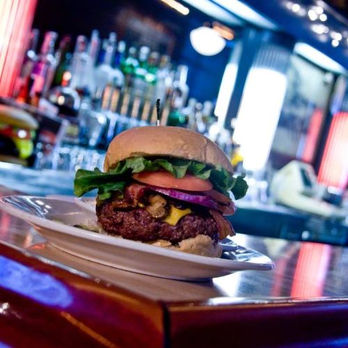 A juicy burger with lettuce, tomato, pickles, and cheese on a plate, set against a vibrant bar background.