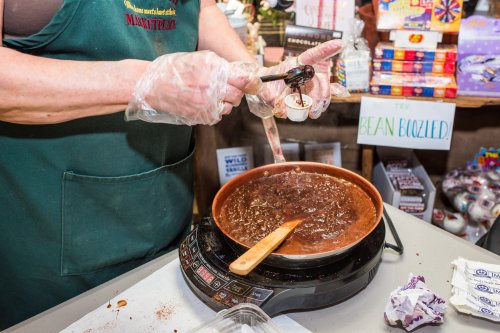 A person in gloves stirs melted chocolate in a pot on a hot plate, preparing a sweet treat.