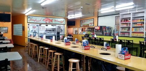 Interior of a seafood market with a long table, stools, and a counter displaying food items and drinks.